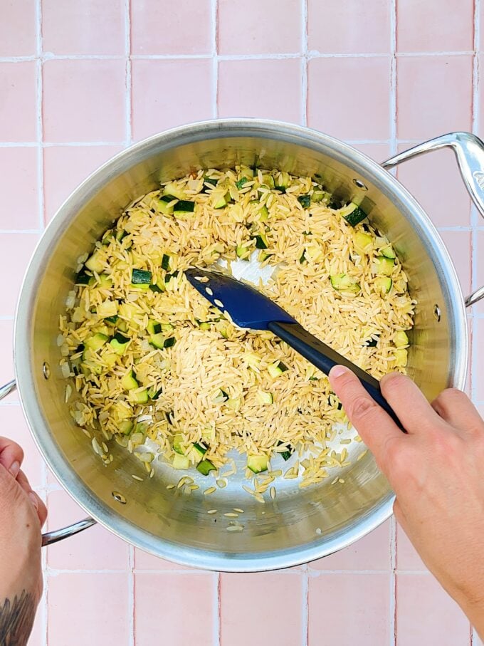 hand stirring orzo in pot