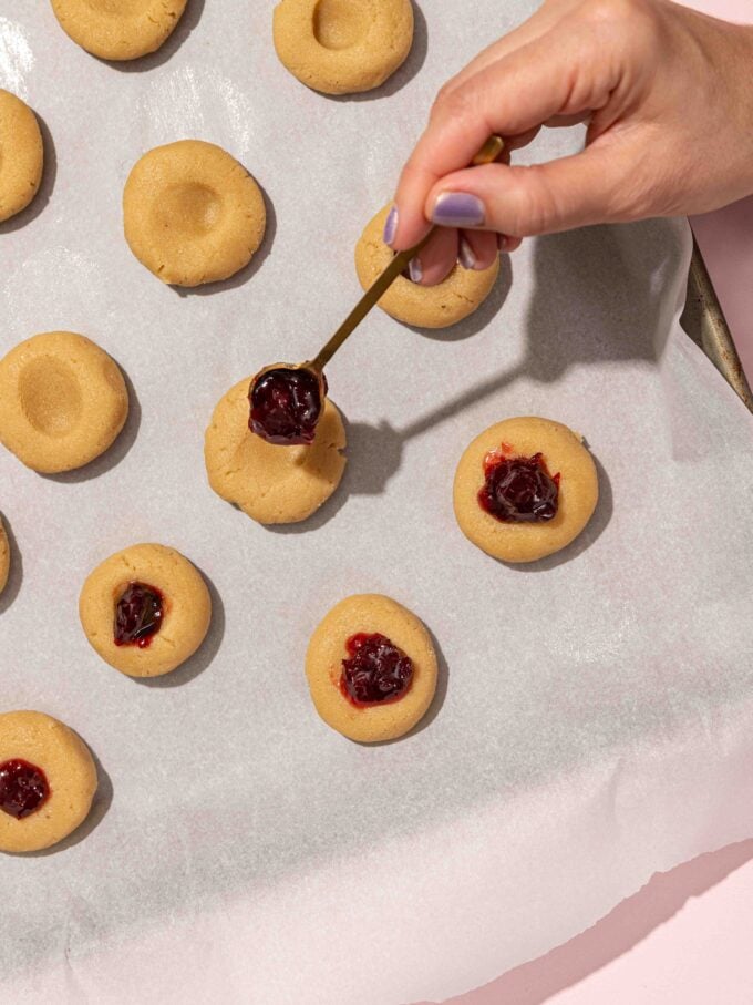 hand spooning jam into thumbprint cookies